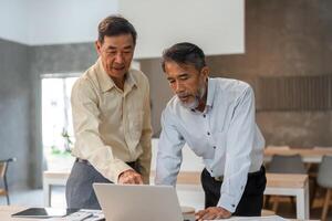 Businessmen collaborating on financial data analysis while pointing at a laptop screen in a modern office photo