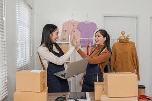 Joyful online sellers giving each other a high-five while reviewing orders on a laptop in their trendy boutique photo