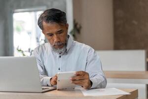 Elderly businessman calculating expenses with calculator in modern office setting photo