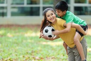 Family Recreation and Soccer Fun. A mother carries her son on her back while he holds a soccer ball, showcasing their active lifestyle. photo