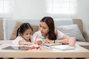 Creative Learning and Parental Support. A child draws while her mother provides guidance, creating a loving atmosphere for education. photo