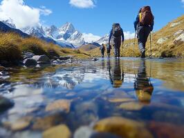 Hikers with Backpacks Crossing Rocky Riverbed with Snow Capped Mountains Under Blue Sky on Sunny Day in Mountainous Landscape photo