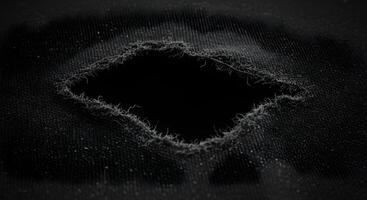 Close-up of ripped black denim fabric, exposing detailed thread patterns and worn-out fibers. Fabric rips texture. photo