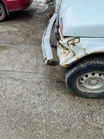un blanco coche ese tiene un dañado parachoque es estacionado en el lado de el camino, tomando arriba espacio y posiblemente atrayendo el atención de paso automovilistas y peatones igual foto