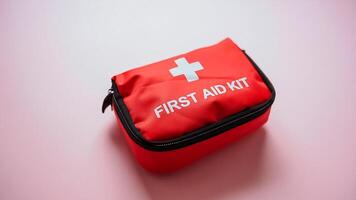 A red first aid kit with a white cross symbol is prominently on a vibrant pink surface, indicating its purpose for health care and emergency assistance, ensuring readiness when needed photo