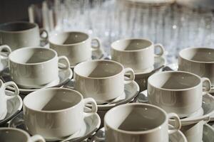 On a table, there is a collection of white coffee cups and their matching saucers, neatly arranged, beckoning for a cozy coffee moment or delightful tea time conversation photo