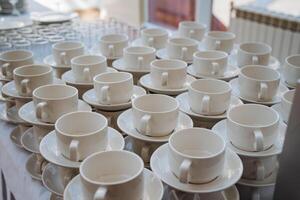 An elegant table is adorned with an abundance of pristine white coffee cups accompanied by matching saucers, creating a delightful setting for enjoying beverages and hospitality photo