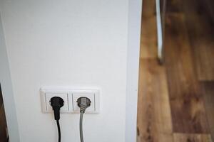 Two electrical plugs are currently inserted into a wall socket, enabling power supply to devices or appliances connected to them for functionality and use in technology applications photo