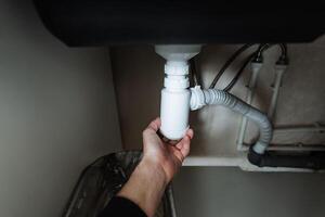 An individual is actively holding a drain pipe positioned underneath a sink, which indicates that they are engaged in important plumbing or maintenance tasks related to home upkeep photo