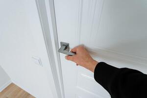 A person is carefully opening a white door that features a shiny silver handle, highlighting the doors design and functionality within the context of their home environment photo