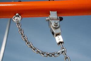 A closeup view showcasing a metal pulley accompanied by a chain, which is mounted on a vibrant orange frame of playground equipment for outdoor fun and interactive activities photo
