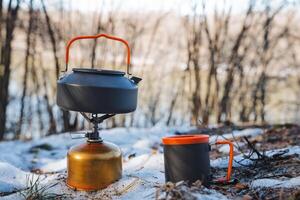 A kettle is placed on top of a gas cylinder, positioned right next to a cup, all resting in the cold snow, creating a unique kitchen scene amidst the wintery surroundings photo