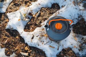 A bright, cheerful tea kettle featuring an orange handle sits prominently atop a large, fluffy pile of pristine, white snow, creating a vivid contrast in color and texture photo