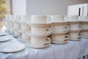 A wellorganized table displays immaculate white cups and saucers, stacked elegantly to highlight their exquisite design and sophistication, creating a striking visual impact photo