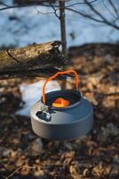 A compact and practical camping kettle hangs from a sturdy tree branch, inviting you to embrace adventure and exploration in the beautiful and vast wilderness surrounding you photo