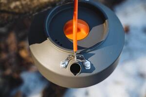 A tea kettle is unexpectedly hanging from a tree branch while surrounded by the beautiful white snow that has blanketed the ground. It creates a striking contrast in the scenery photo