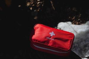 A bright red first aid kit is sitting prominently on top of a substantial pile of soft, white snow, ready to provide necessary medical assistance when needed in cold weather conditions photo
