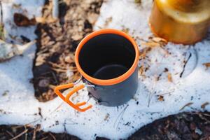 A cup featuring a vibrant orange handle is currently resting atop a blanket of soft snow, creating a striking contrast against the white backdrop of the winter landscape photo