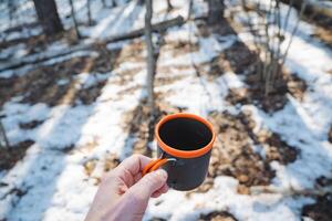 A person is standing outside in the beautiful snow while holding a warm cup of delicious coffee, creating a comforting and cozy contrast against the chilly winter landscape surrounding them photo