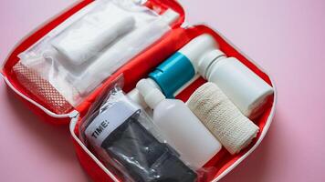 A bright red first aid kit that is filled to the brim with various bottles and an assortment of bandages, all set against a vibrant pink background that adds a cheerful touch photo