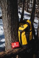 A bright yellow hiking backpack and a wellstocked first aid kit positioned strategically on a tree against the picturesque backdrop of a snowy forest landscape photo