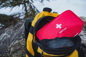 A vibrant yellow backpack is filled with essential items for various needs, including a bright red first aid kit that ensures easy and quick access during emergencies or outdoor activities photo