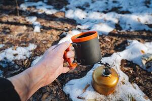 A person is standing outside in the snow, holding a warm cup of coffee in their hands, enjoying the chilly scenery while sipping on their drink. It is quite a lovely sight photo