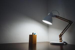 A desk lamp is on a table next to a pen photo