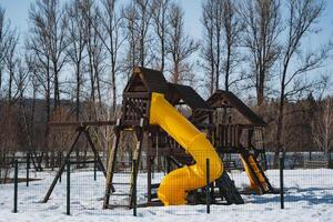 In the center of a snowy playground, there is a brightly colored yellow slide, which stands out amidst the cold white snow covering the ground, making it look both inviting and cheerful photo