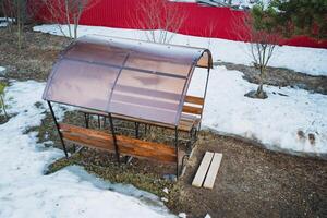 A sturdy wooden bench, complemented by a plastic roof, is currently resting in a thick layer of snow, showcasing an interesting juxtaposition of materials and natures beauty photo