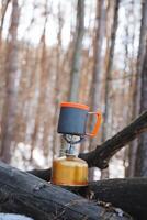 A traditional gas stove is positioned on a robust and sturdy log located in a serene woodland setting, with a cup carefully balanced on top, forming a beautifully picturesque natural scene photo