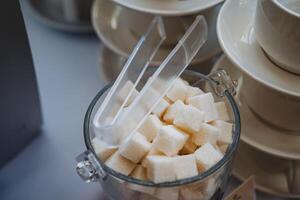 This elegant glass jar filled with sweet sugar cubes and tiny tongs adds practicality and charm to any kitchen or dining table, enhancing your culinary space and aesthetic appeal photo