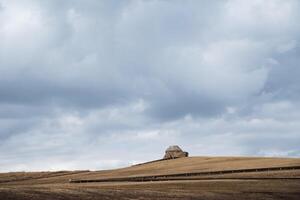 There is a quaint and small building perched atop a picturesque hill, beautifully contrasted against a cloudy sky that stretches across the background, creating a serene environment photo