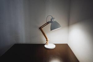 In a dimly lit room, a stylish desk lamp perfectly positioned on a beautifully crafted wooden table emits a warm, inviting glow that enhances the overall ambiance of the space photo