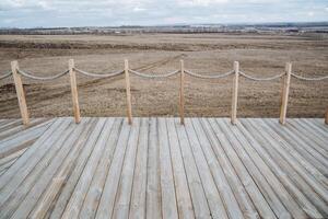 A beautiful wooden deck complete with a sturdy rope fence that offers a stunning view of a vast, open field stretching out before you, creating a sense of serenity and connection to nature photo