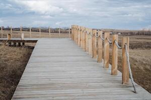 A beautifully crafted wooden walkway that gracefully leads into an expansive field, complemented by a sturdy rope fence that enhances its rustic charm and natural appeal photo