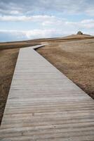There is a beautifully crafted wooden walkway that leads up a gentle hill, situated in the heart of a sprawling field, offering a scenic route for all who venture through the landscape photo