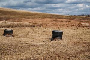 In a sprawling and expansive open field, two distinct barrels prominently stand out against the natural landscape, likely intended for the storage or disposal of various items and materials photo