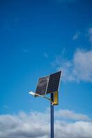 In the foreground, there is a solar panel securely mounted on a tall pole, and in the background, the sky shines bright and blue, creating a picturesque scene of renewable energy photo