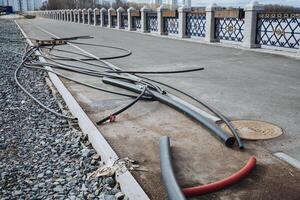 A messy and tangled mass of various wires is carelessly spread out on the ground near a bridge, which poses a significant hazard to pedestrians and passersby who may be in the area photo
