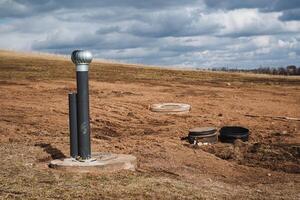 In the center of a barren dirt field, there is a prominent black pipe that is clearly visible, standing out against the brown backdrop of the soil and dry land around it photo