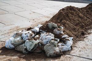 A large pile of dirt is resting on the ground, situated right next to an adjacent pile that consists of bags filled with dirt, both of which are contributing to local pollution issues photo
