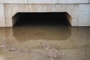 Beneath a bridge lies a significant concrete tunnel that is entirely filled with water, resulting in a fascinating landscape that is visually captivating and draws attention from onlookers photo