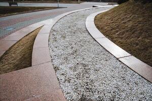 A beautifully designed curved walkway features gravel elegantly lining its side, enhancing the aesthetic and functionality of the public space while providing a pleasant walking experience photo