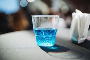 A plastic cup, brimming with a vibrant blue liquid, is placed on a table, catching the eye with its striking color and simple elegance, perfect for serving cold beverages photo