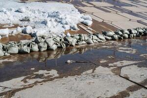 A small puddle of water sits quietly nestled amidst several bags of sand, creating an intriguing visual contrast against the chilly backdrop of the winter season and its wintry charm photo