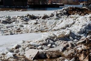 A substantial pile of ice is resting on the ground adjacent to a large body of water, creating a striking scene that highlights the beauty of winters cold and frosty essence photo