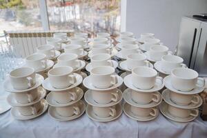 This meticulously arranged table beautifully showcases elegant white cups accompanied by matching saucers, coming together to create a chic serveware set suitable for various beverages photo