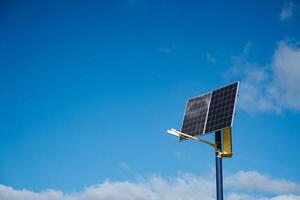In the image, there is a solar panel mounted on a tall pole, and it is set against a vibrant blue sky that adds a beautiful contrast, emphasizing renewable energy technology photo