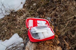A bright red first aid kit is positioned conveniently on a sturdy tree stump located in the forest, ensuring quick access for emergencies that may arise during nearby outdoor activities photo